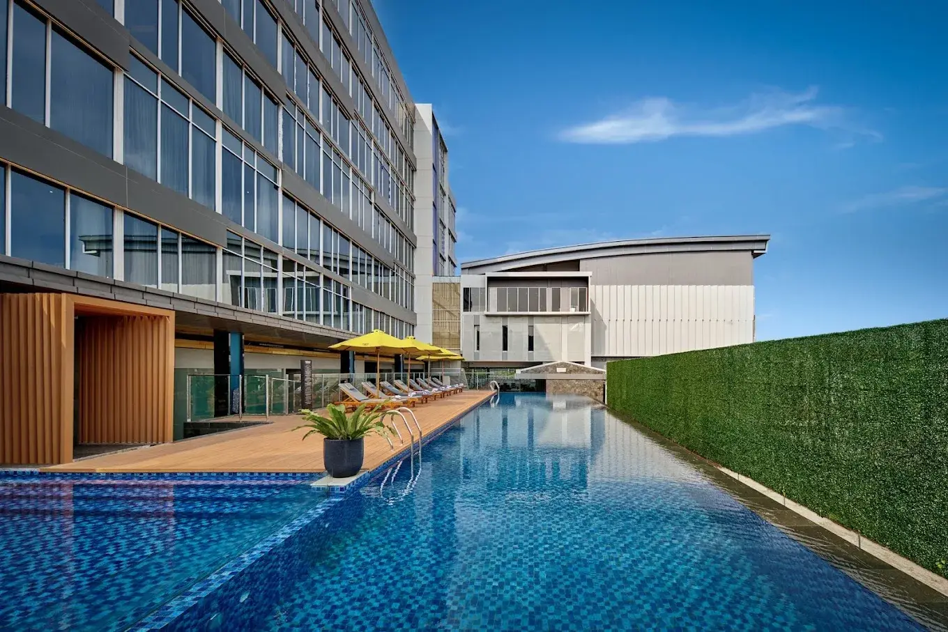 Tampak area kolam renang dan fasad Hotel Voco di Bandung dengan bidang kaca dan panel pada bangunan.