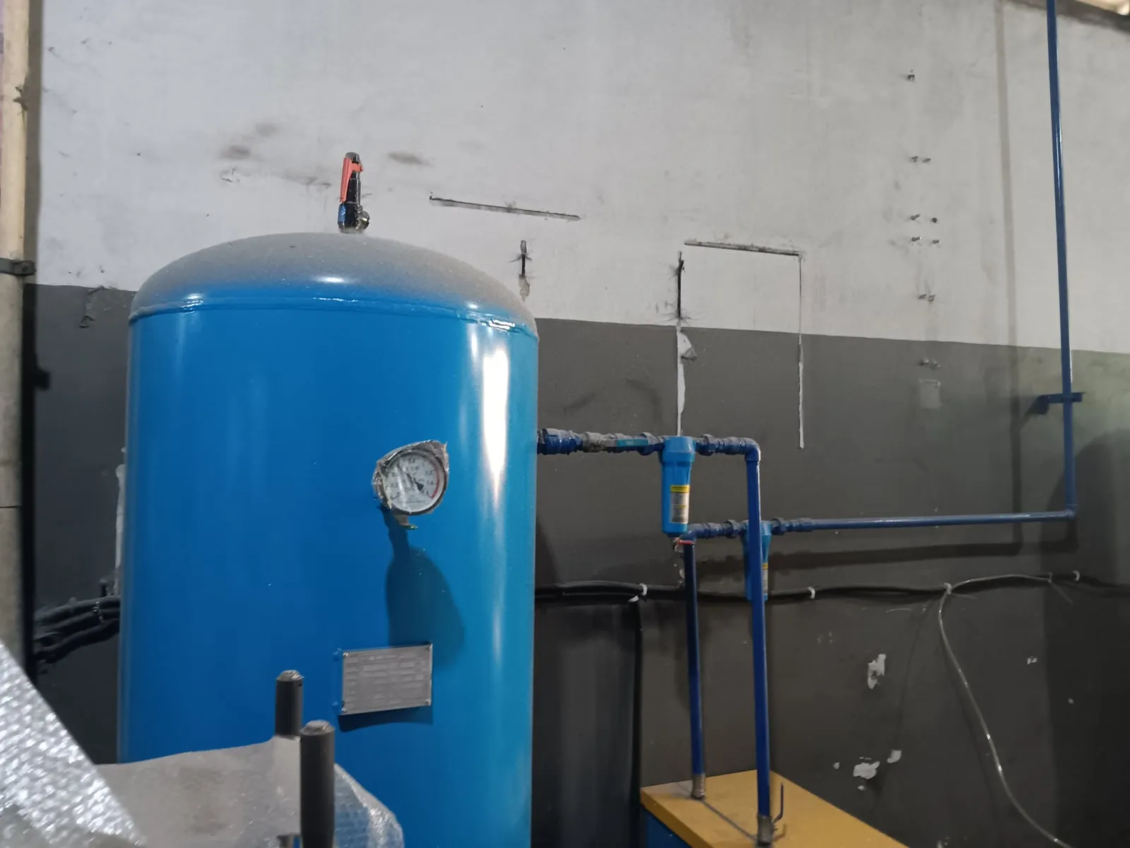 Kompresor dengan tangki biru dan jaringan pipa di workshop
