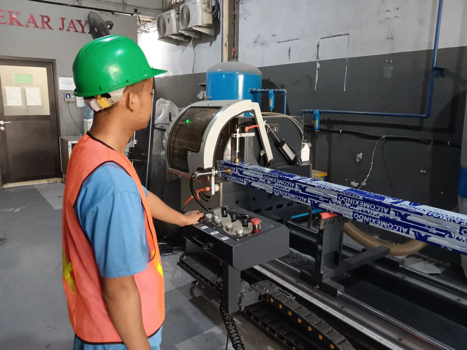 Pekerja mengoperasikan mesin potong Demac dengan profil aluminium di workshop